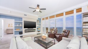 Ein großzügiges Wohnzimmer mit einem großen Flachbildfernseher, bequemen Sitzmöglichkeiten und einem Balkon mit Meerblick.