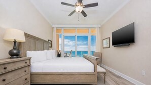 A hotel room with a bed, a television, a ceiling fan, a nightstand, and a view of the ocean. - Phoenix Gulf Towers 1105 4 Bedroom Condo (Orange Beach)