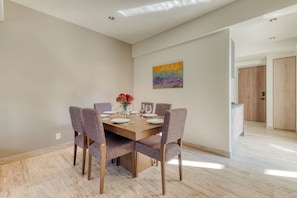 A dining area with a wooden table and six chairs, a vase with flowers, and a colorful painting on the wall.