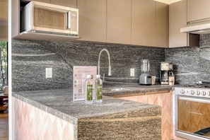 A kitchen with a granite countertop, a built-in microwave, a coffee maker, and a stove.