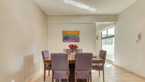 A dining area with a wooden table and chairs, a vase with flowers, and a colorful painting on the wall.