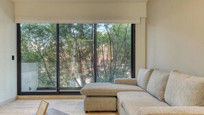 A modern living room with a large window, a sectional sofa, a wooden coffee table, and a framed picture.