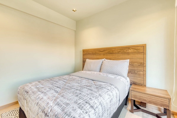 A bedroom with a bed, a wooden headboard, a nightstand, and a wall-mounted light fixture.