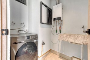 A laundry room with a front-loading washing machine, a wall-mounted heater, and a sink with a towel rack.