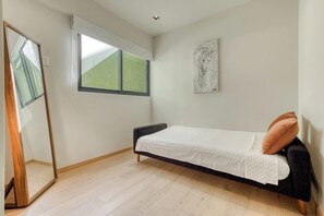 A small bedroom with a single bed, a window, a mirror, and a wall-mounted artwork.