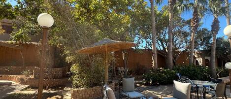 An outdoor patio area with stone walls, palm trees, and a seating arrangement including tables and chairs.