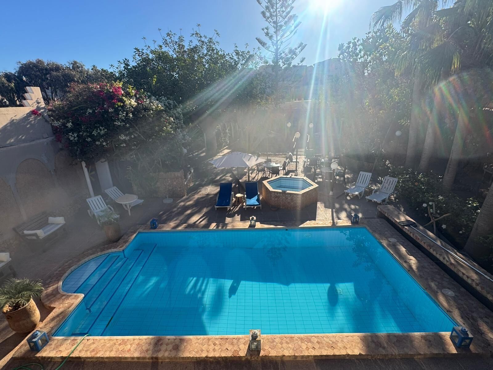 Une piscine rectangulaire, bordée d’une terrasse carrelée, entourée de chaises longues et d’un jacuzzi.