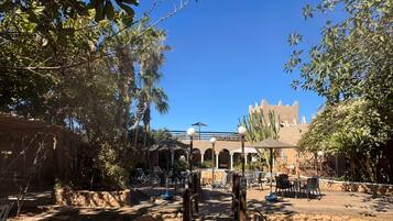 An outdoor seating area with tables and chairs, surrounded by trees and a clear blue sky.