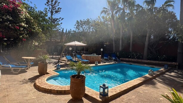 A pool area with lounge chairs, a small table, and potted plants. - LES ETOILES DU KSAR (Mirleft)