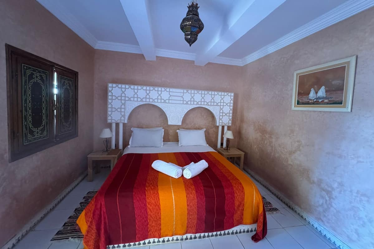 A hotel room with a large bed, two nightstands, a decorative headboard, a hanging lantern, and a framed picture on the wall.