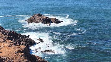 A coastal landscape with rocky formations and waves crashing against them.