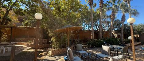 An outdoor seating area with tables and chairs, surrounded by palm trees and a stone wall.