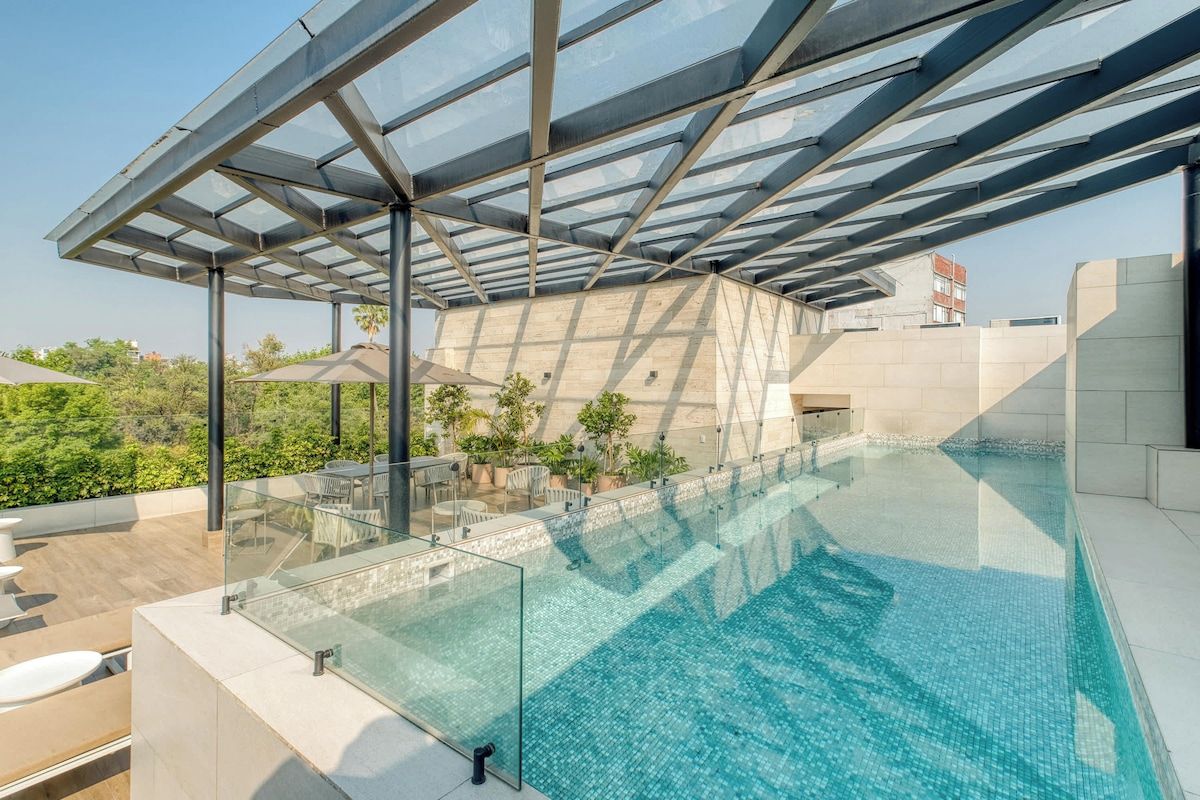 A rooftop infinity pool with a glass barrier, surrounded by outdoor seating and plants.