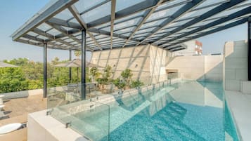 A rooftop infinity pool with a glass barrier, surrounded by outdoor seating and plants.