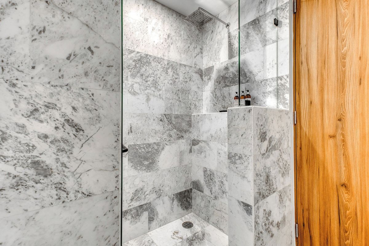 A shower with marble tiles and a wooden door.