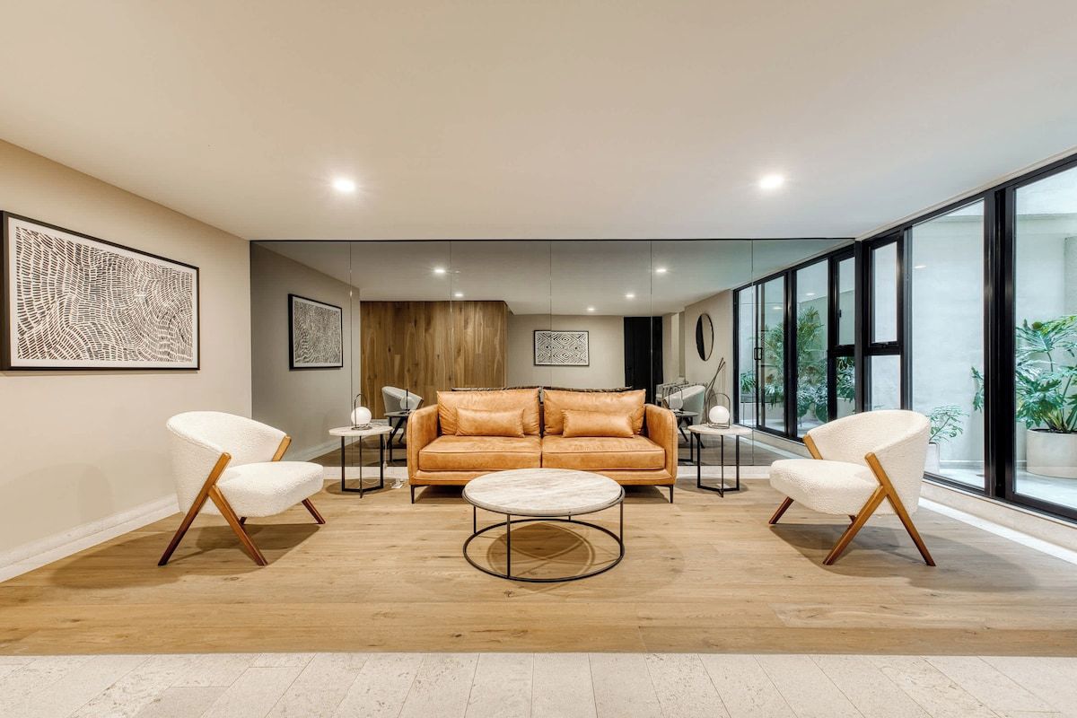 A modern living room with a leather sofa, two white armchairs, a round coffee table, and artwork on the walls.
