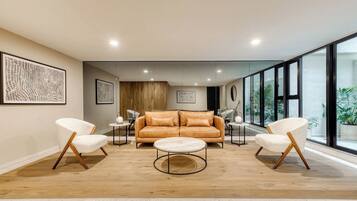A modern living room with a leather sofa, two white armchairs, a round coffee table, and artwork on the walls.