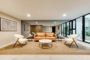 A modern living room with a leather sofa, two white armchairs, a round coffee table, and artwork on the walls.