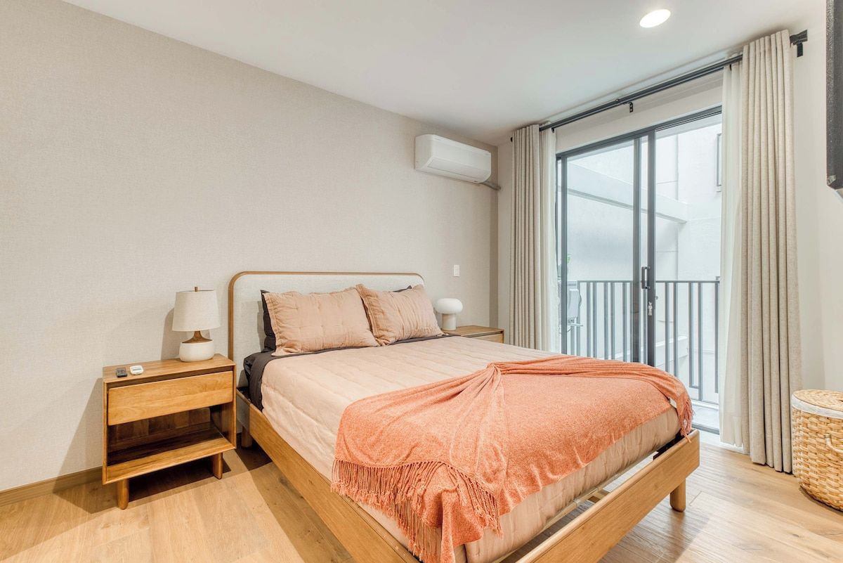 A bedroom with a bed, nightstand, and a window with curtains.