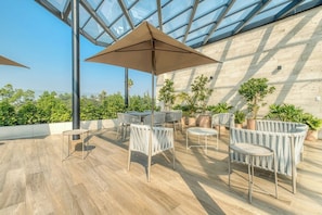 An outdoor patio with tables and chairs, a glass ceiling, and potted plants.