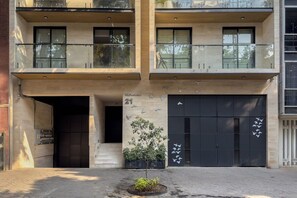 Un immeuble à plusieurs étages, avec une entrée au niveau du sol, un petit arbre et le chiffre « 21 » peint sur le mur.