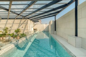 Une piscine dotée d’un toit en verre, entourée de murs recouverts de carreaux et agrémentée de plantes en pot.
