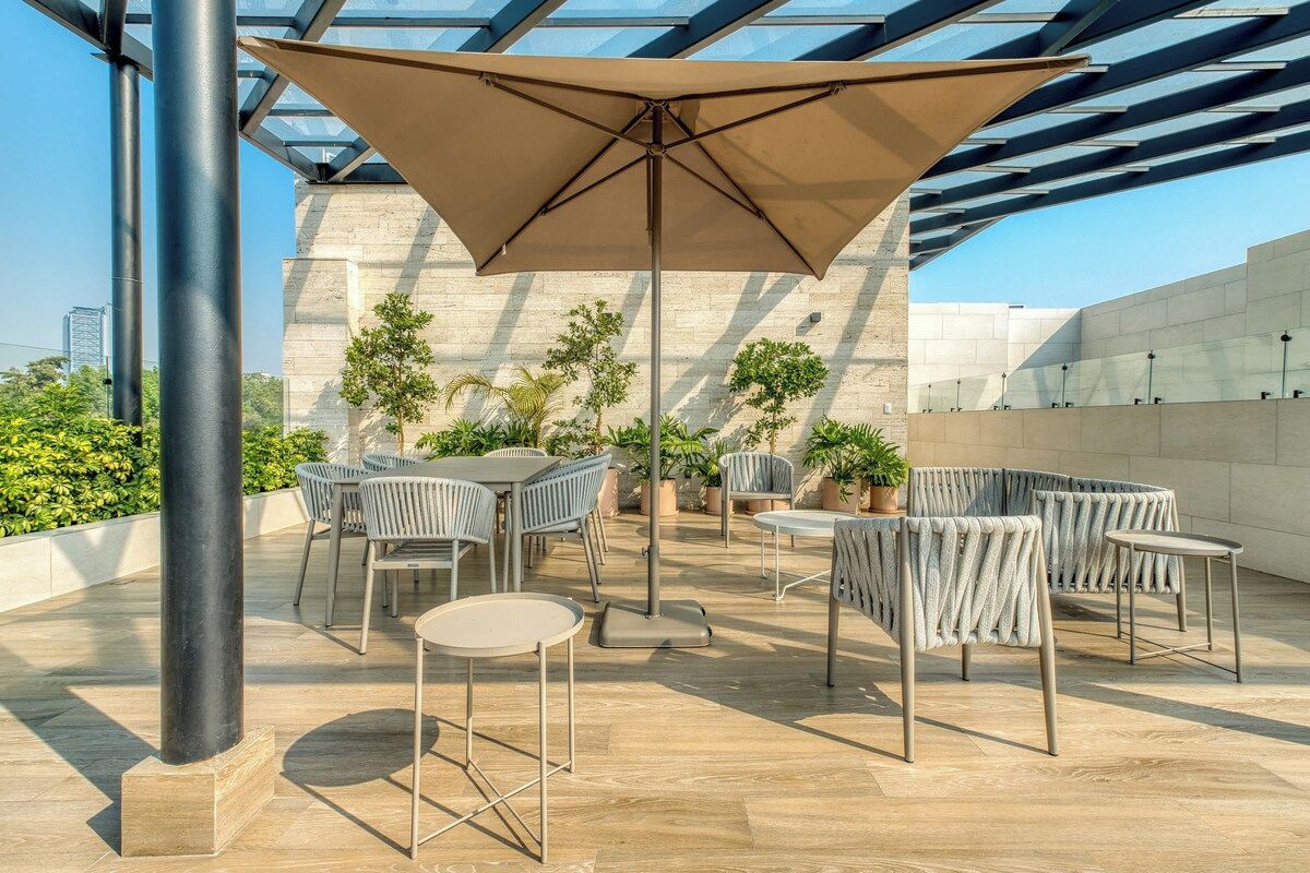 Une terrasse extérieure avec des tables et des chaises, un grand parasol et des plantes en pot.