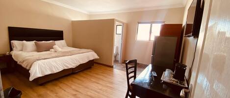 A bedroom with a bed, a desk, and a chair. There is a window and a door leading to a bathroom.