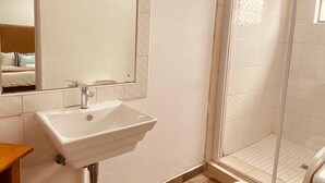 Egy fürdőszoba, amelyben mosdókagyló, tükör, zuhanyzó és WC található.