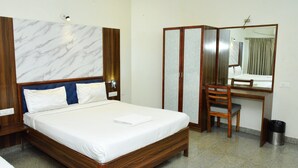 A hotel room with a large bed, a wooden desk, a chair, a mirror, and a wardrobe. - Sri Sai Residence (Tumkur)