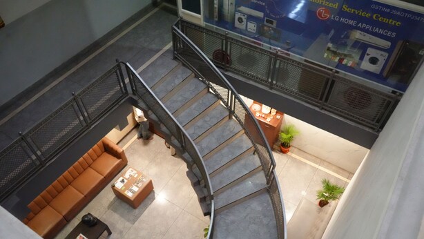 A spacious lobby with a curved staircase, a seating area with a sofa and coffee table, and a display of home appliances. - Sri Sai Residence (Tumkur)