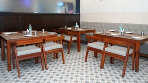 A conference room with wooden tables and chairs, a grey cushioned bench, and a tiled floor. - Sri Sai Residence (Tumkur)