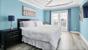 Une chambre à coucher comprenant un lit, une table de chevet, une lampe, un ventilateur de plafond et une fenêtre avec des rideaux.