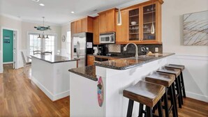 Une cuisine moderne avec des meubles en bois, un îlot central doté de tabourets de bar, un four à micro-ondes et un réfrigérateur.