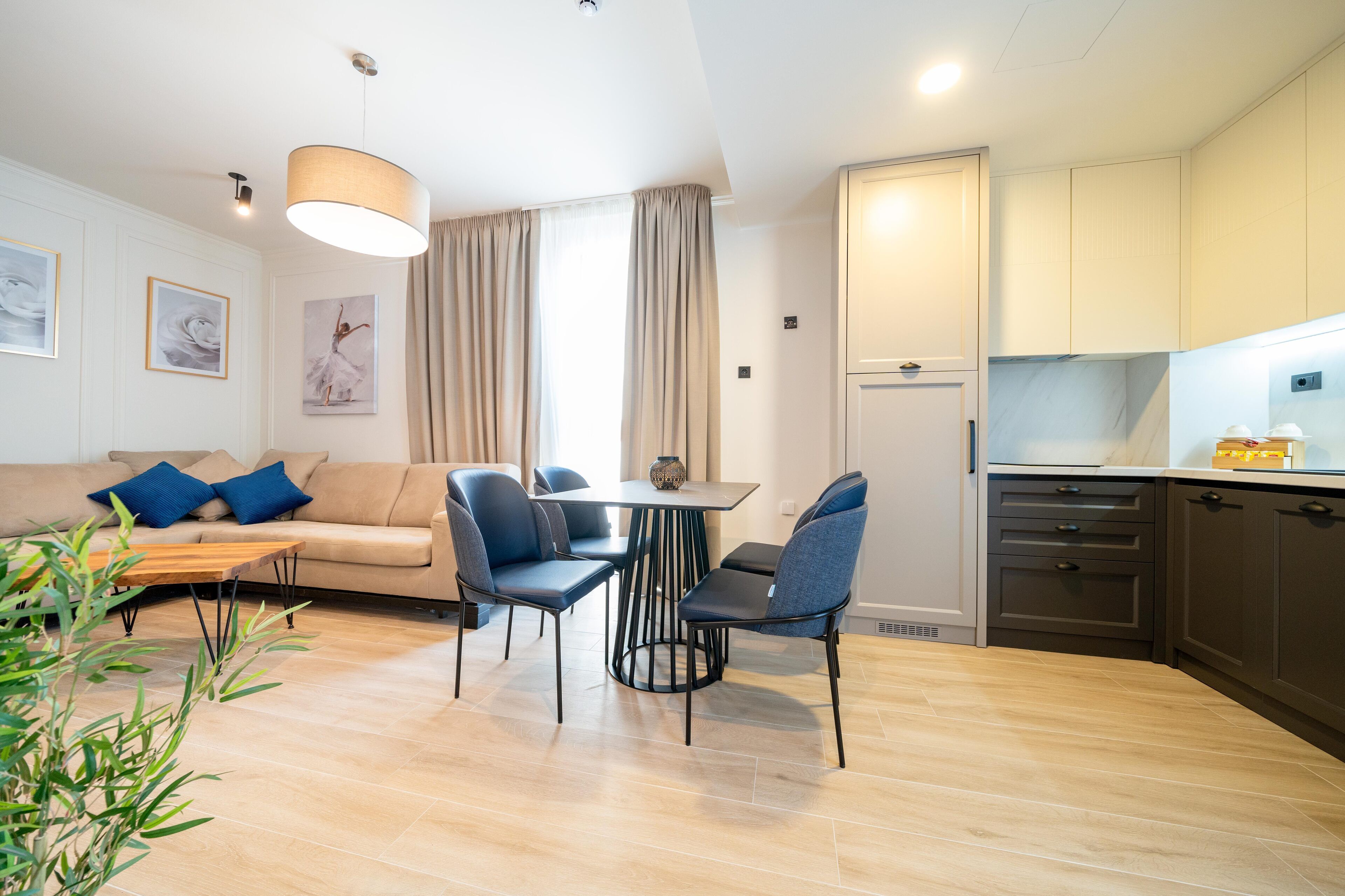 Una sala de estar moderna con un sofá, una mesa de comedor y sillas. Cuenta con una zona de cocina con armarios y una encimera.
