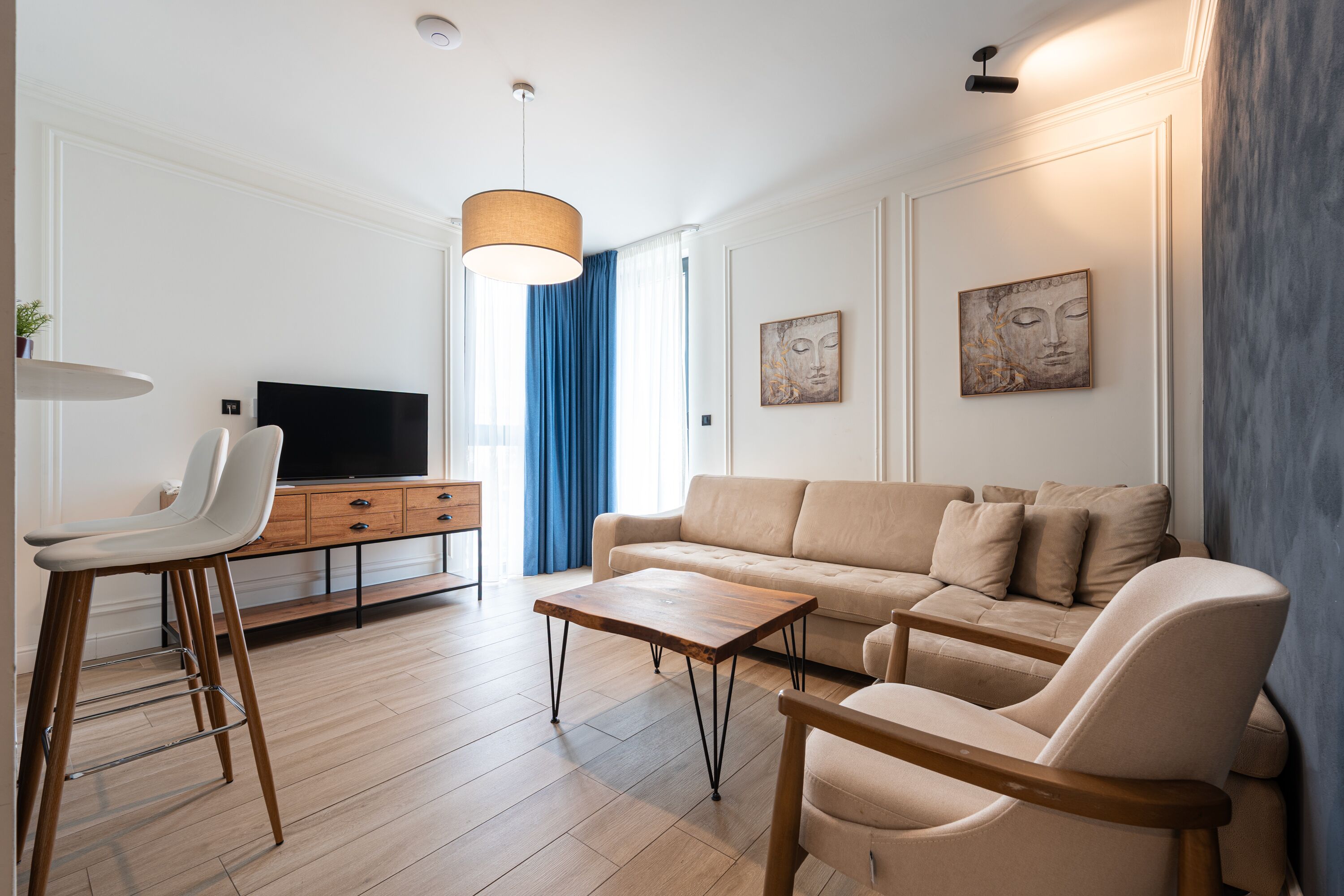 Una sala de estar moderna con un sofá, dos sillones, una mesita de centro, un televisor y una lámpara colgante.