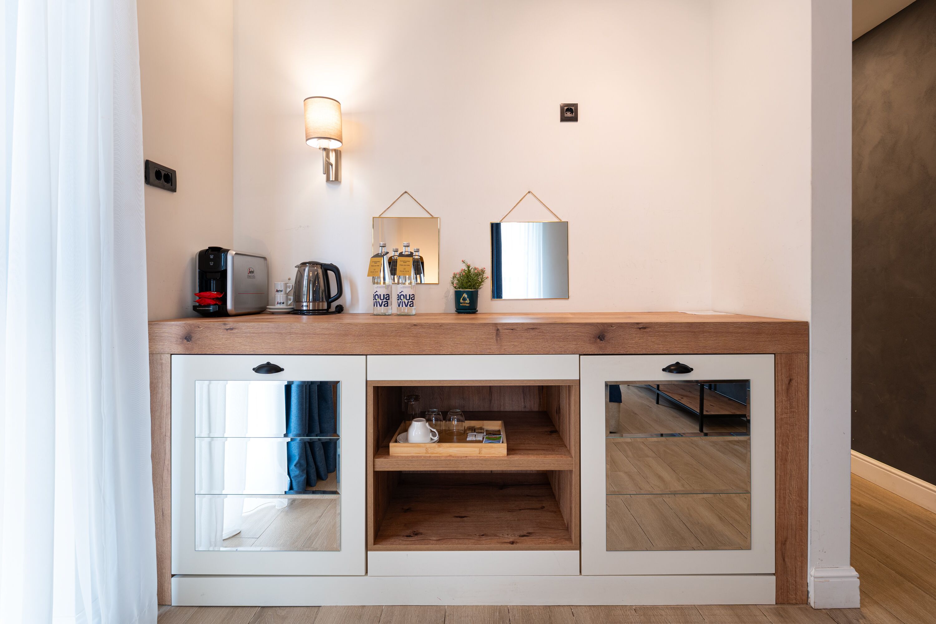 A modern kitchenette with a coffee maker, toaster, and a mirror above a wooden counter.
