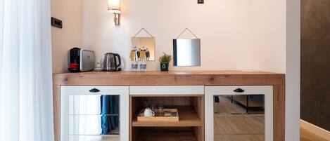 A modern kitchenette with a coffee maker, toaster, and a mirror above a wooden counter.