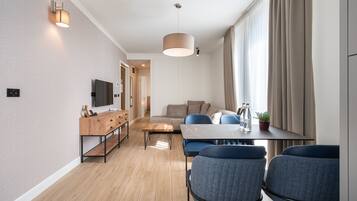 A modern living room with a sofa, a dining table with chairs, a wooden coffee table, and a TV mounted on the wall.