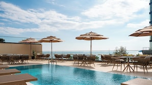 A pool area with lounge chairs and umbrellas, overlooking a body of water. - Hotel Invictus (Becici)