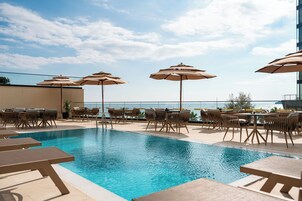Una piscina al aire libre, sombrillas, sillones reclinables de piscina