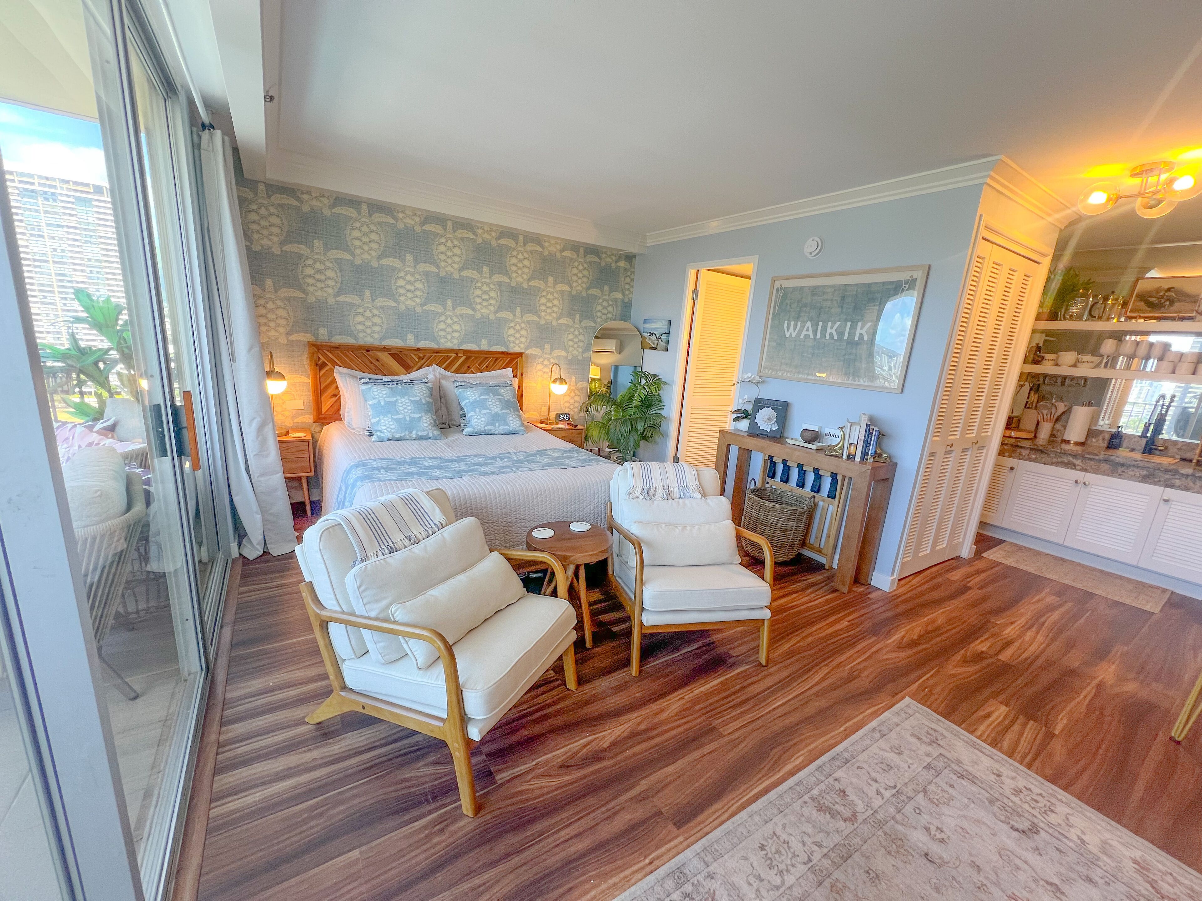 A spacious bedroom with a large bed, two armchairs, a small table, and a console table with decorative items.