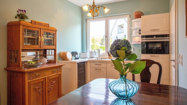 A modern kitchen with wooden cabinetry, a dining table, and a blue vase with a plant. - Penta Apartments (Gamlitz)