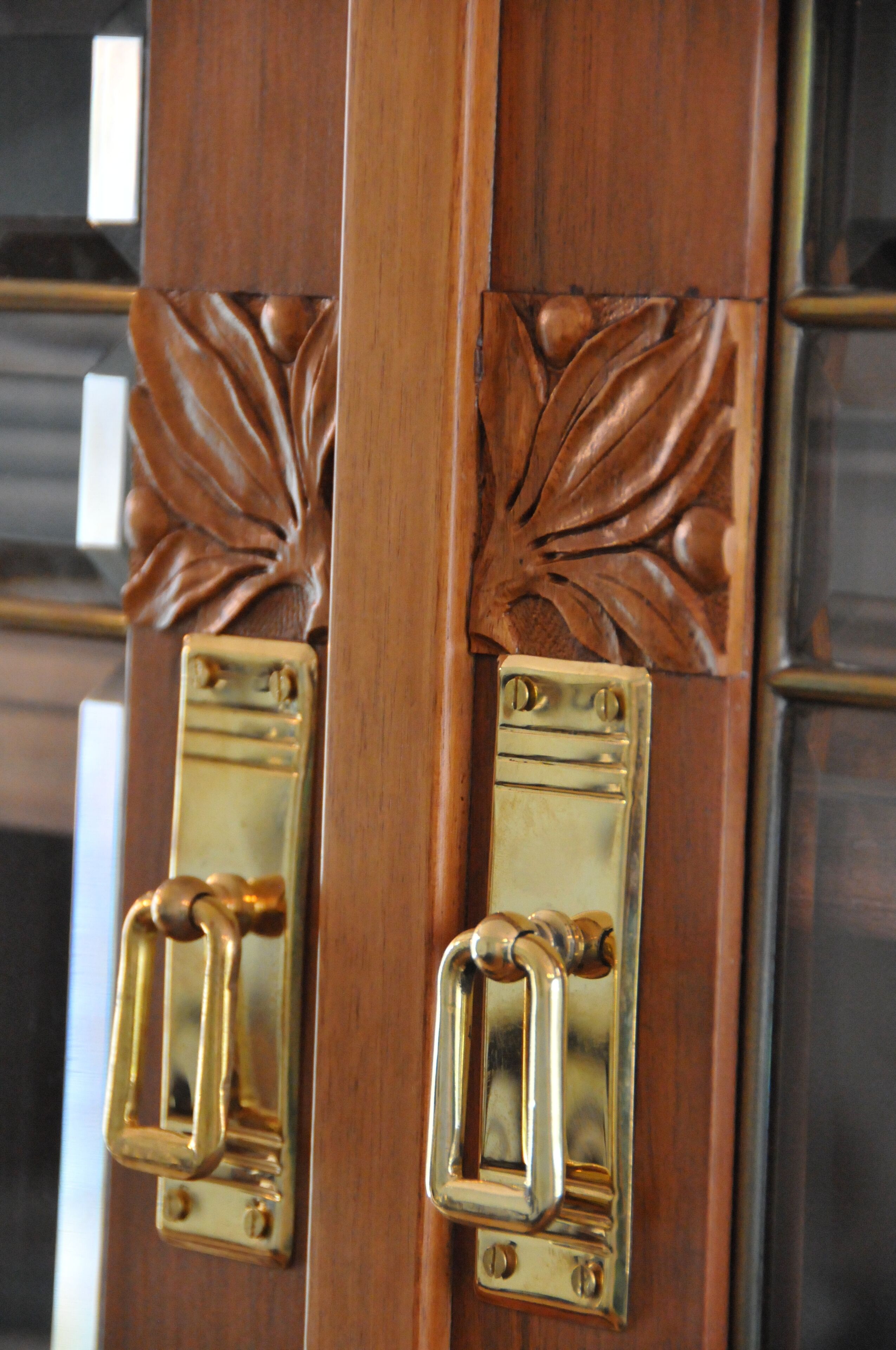 Puerta de madera con dos aldabas de bronce y detalles decorativos de hojas.
