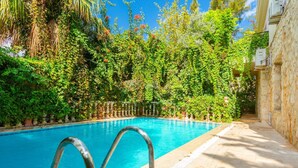 A swimming pool with metal ladders, surrounded by lush greenery and stone walls.