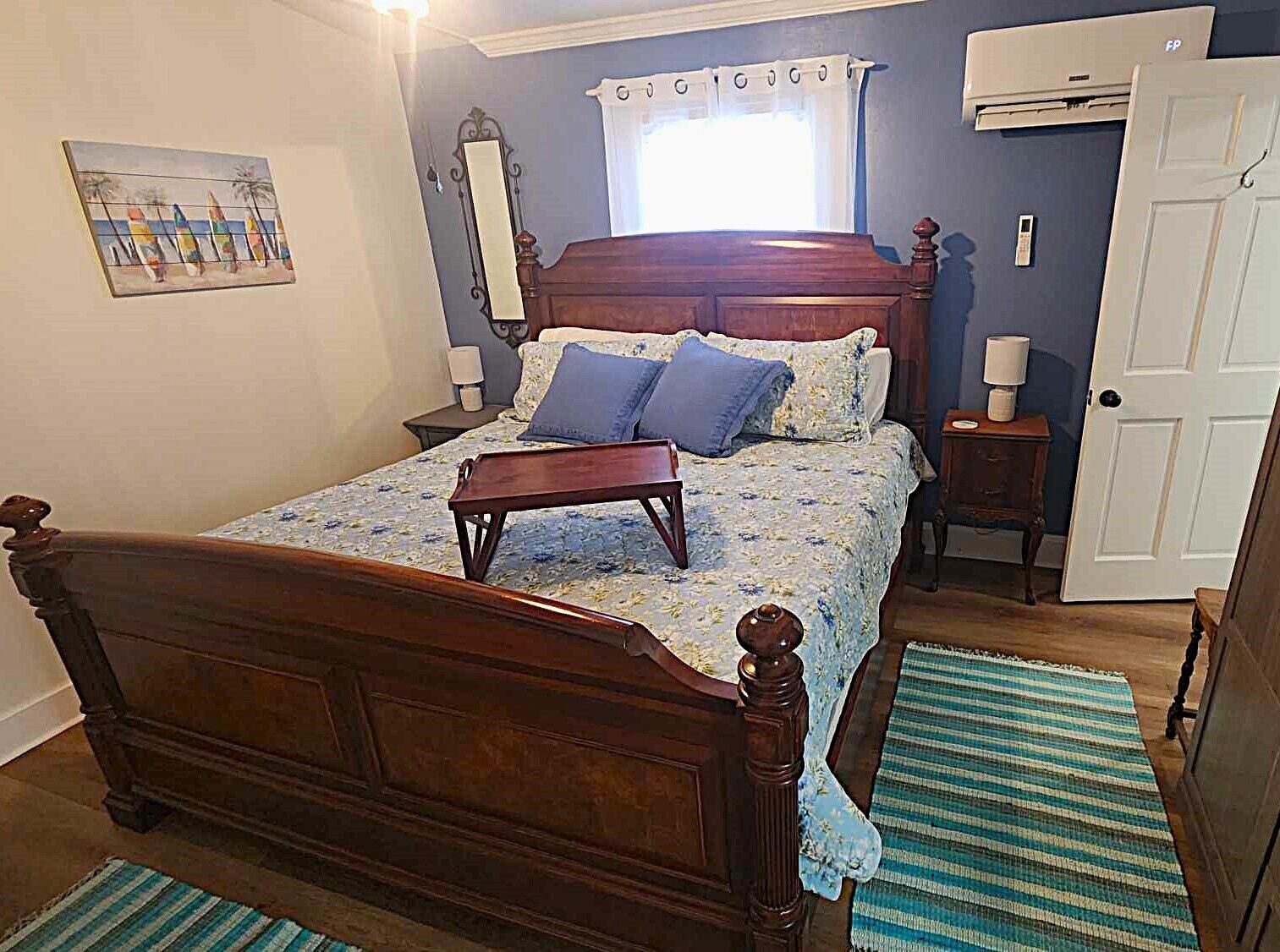 Un dormitorio con una cama de madera, una mesita de noche, una ventana con cortinas, una puerta y un aire acondicionado instalado en la pared.