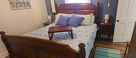 Un dormitorio con una cama de madera, una mesita de noche, una ventana con cortinas, una puerta y un aire acondicionado instalado en la pared.