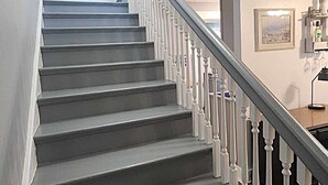 A staircase with white balusters and a dark gray finish, leading to a landing with a framed quote on the wall.