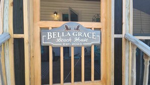 A wooden sign with the text "Bella Grace Beach House" and "EST. 2023" indicating the name and establishment year of the property.
