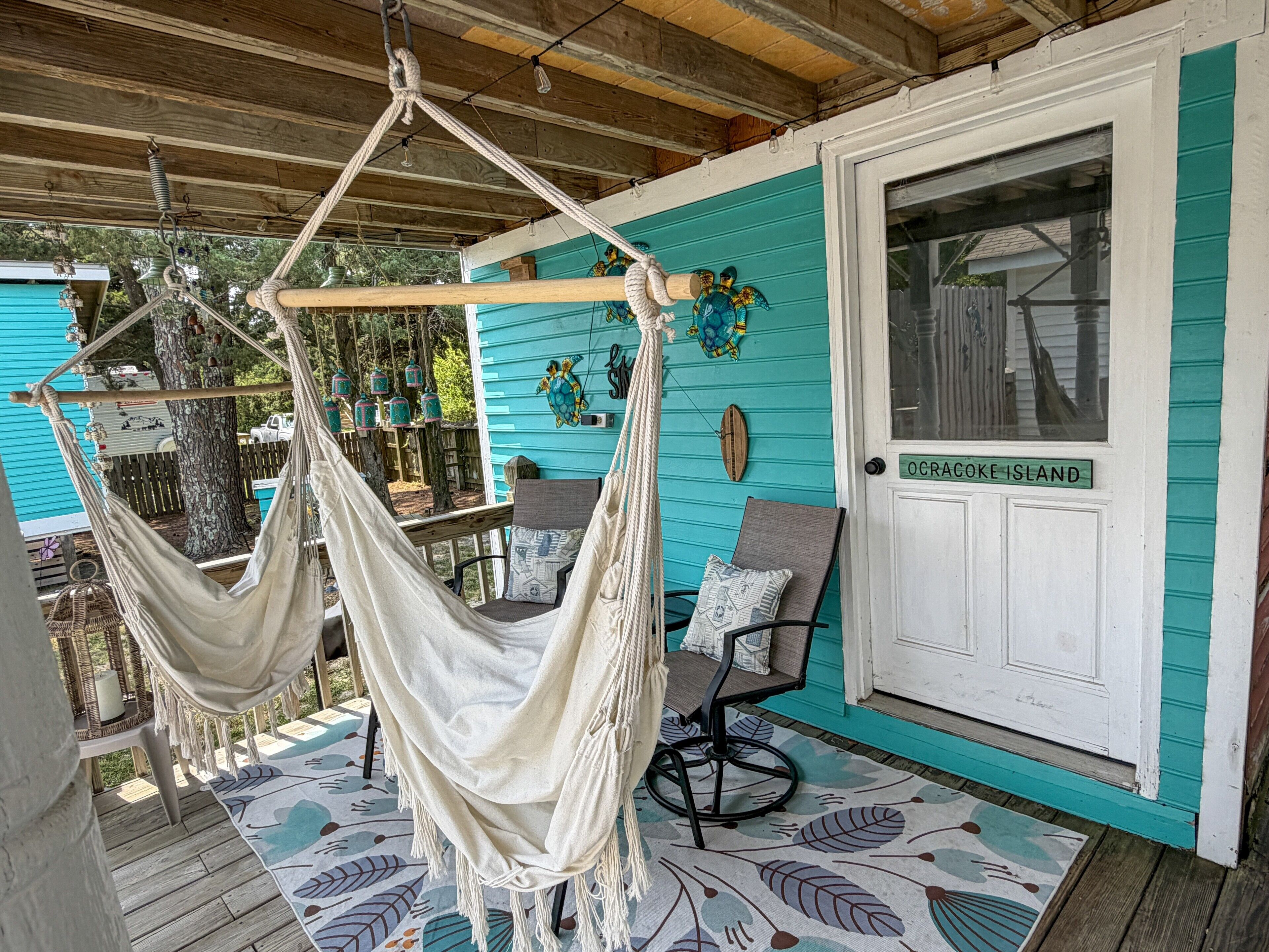 Ein Hängestuhl auf einer Veranda mit einer türkisblauen Wand und einer Tür mit der Aufschrift 'OCRACOKE ISLAND'.